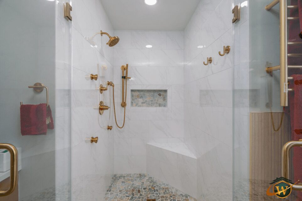 Elegant white shower with gold fixtures and a built-in seat.